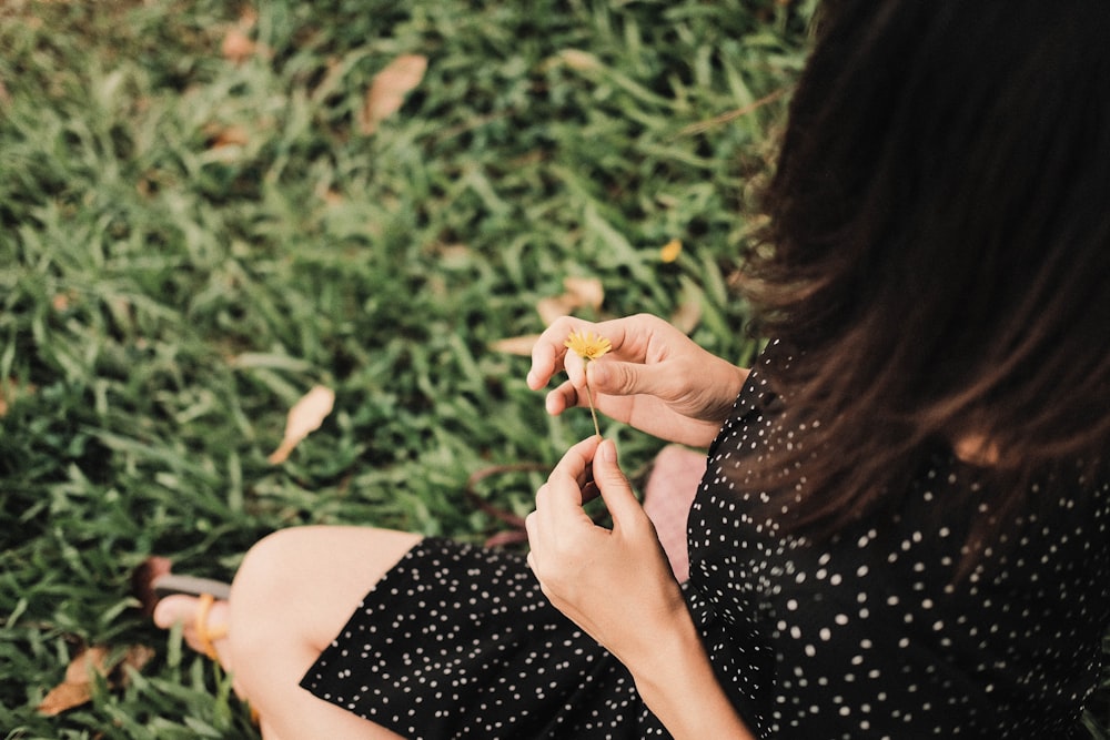 woman in black and white polka dot dress holding yellow flower