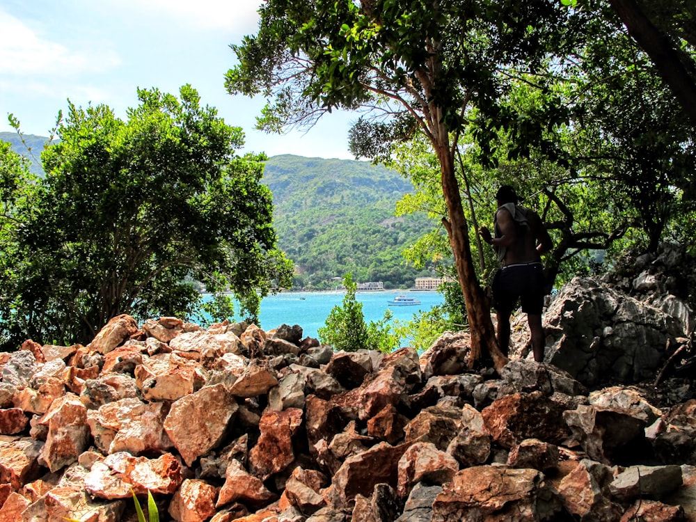 man in black shirt standing on brown rock near body of water during daytime