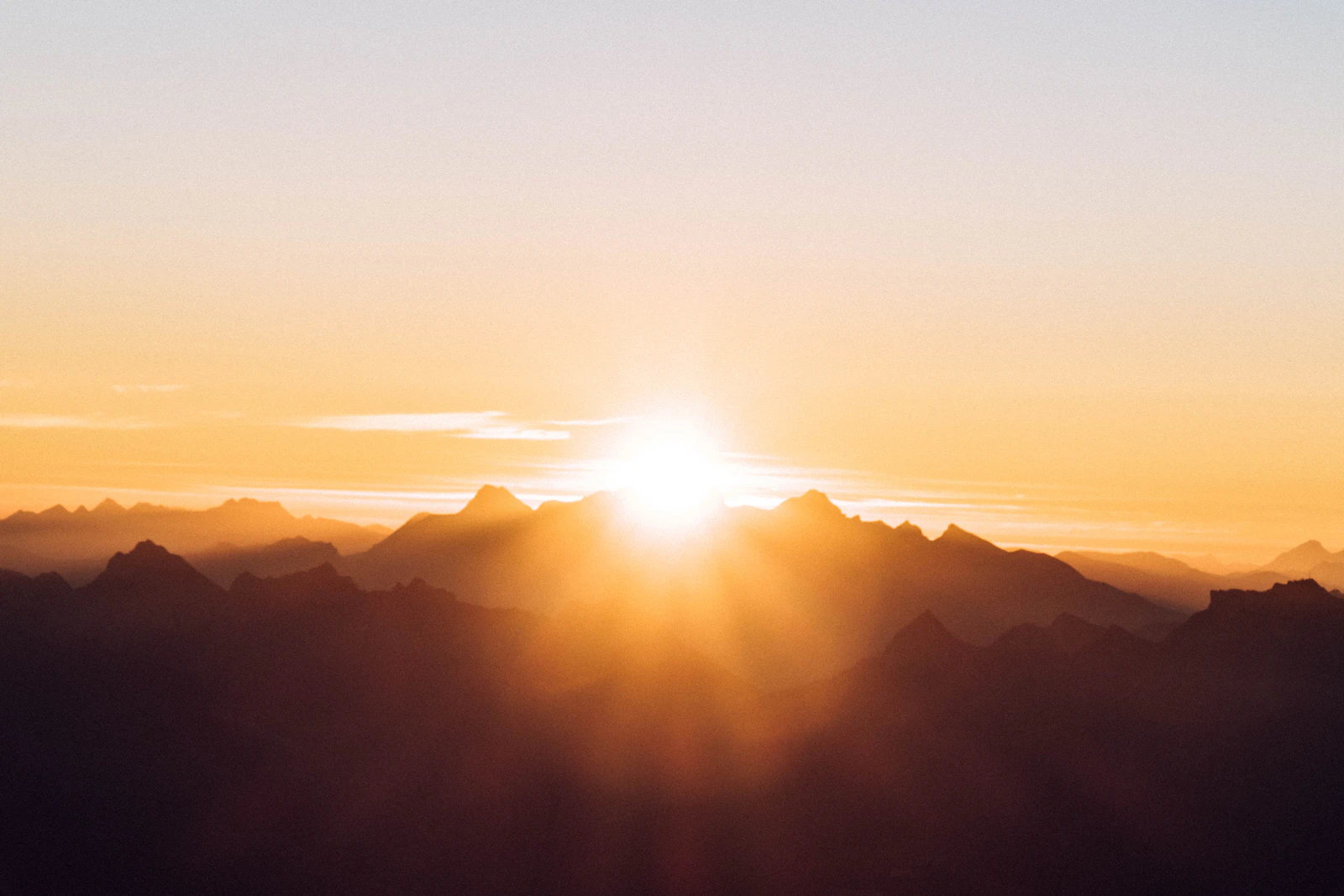 The sun low over a mountain ridge, lighting the sky gold