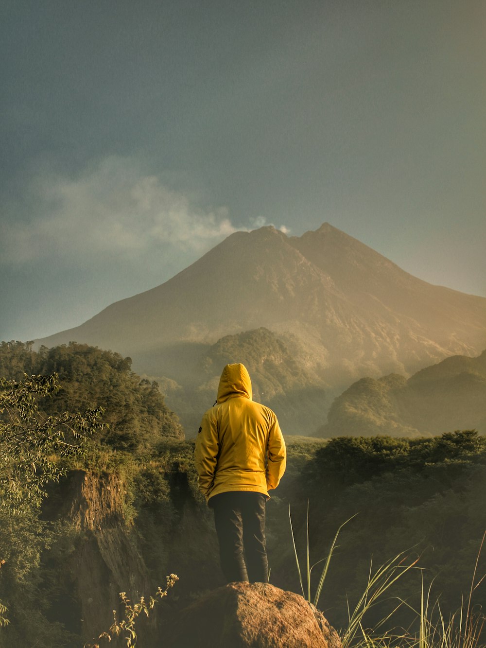 person in yellow hoodie standing on green grass field near mountain during daytime