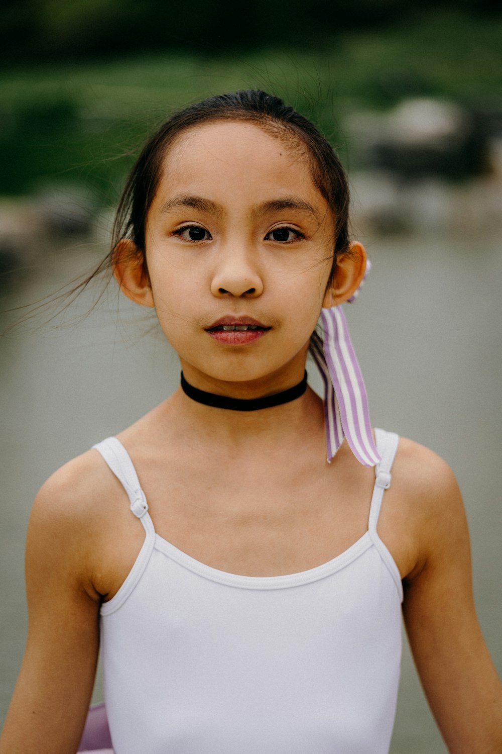 a young girl in a white tank top with a pink ribbon around her neck