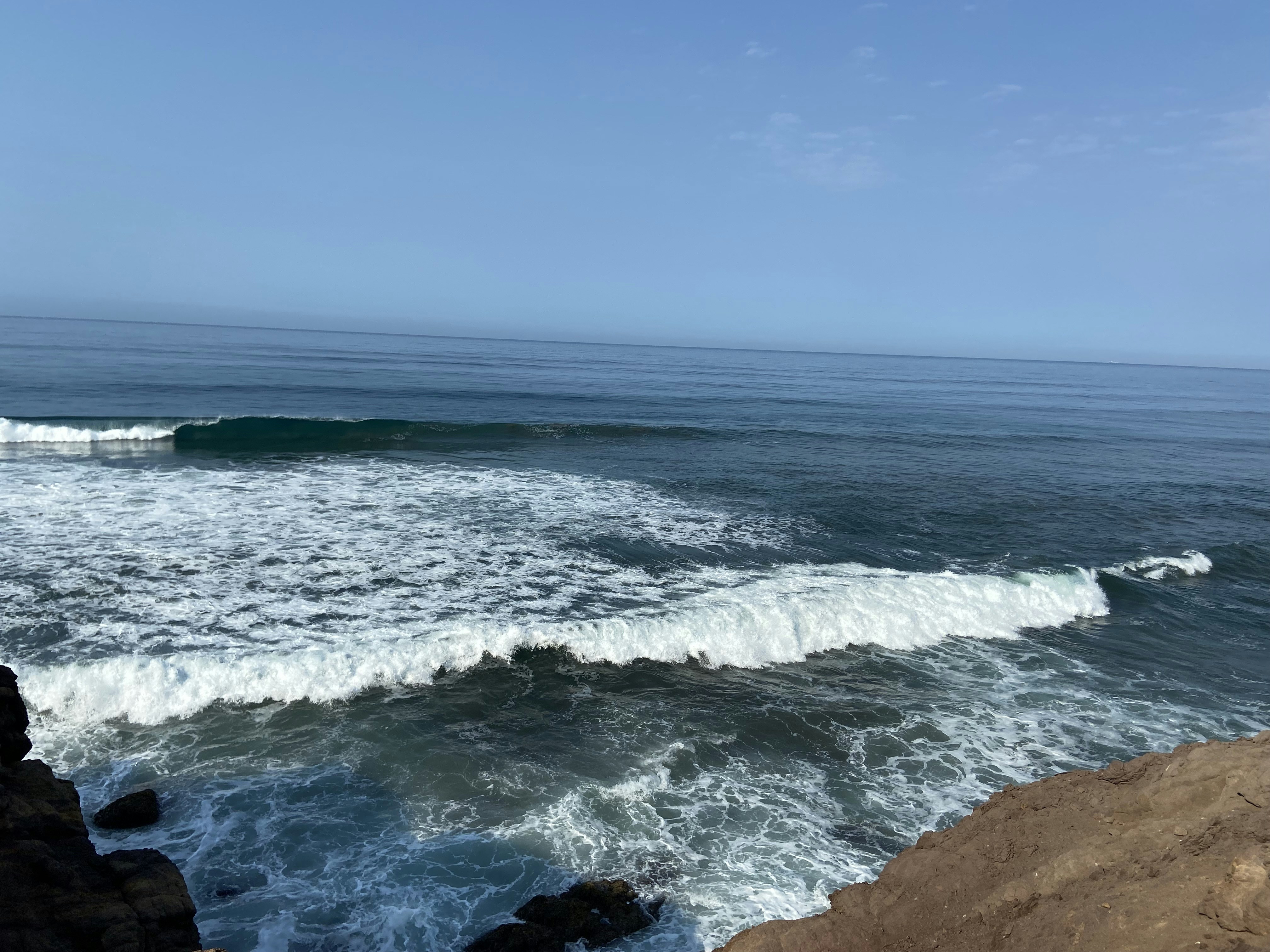 ocean waves crashing on brown rock formation under blue sky during daytime