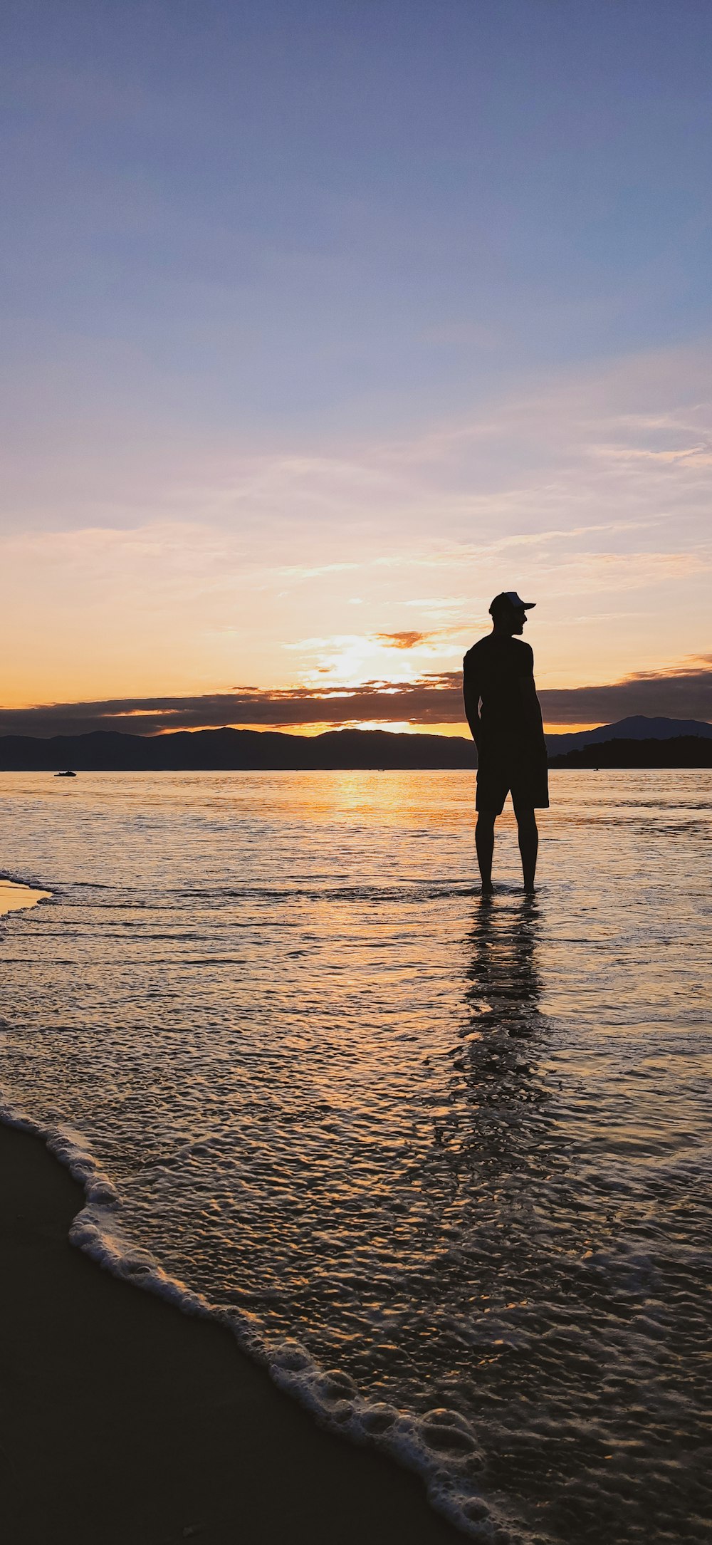 silhouette of man standing on sea shore during sunset