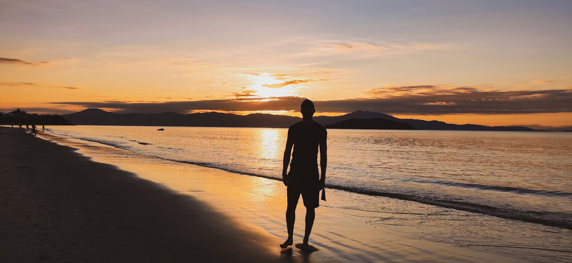 silhouette of man standing on seashore during sunset