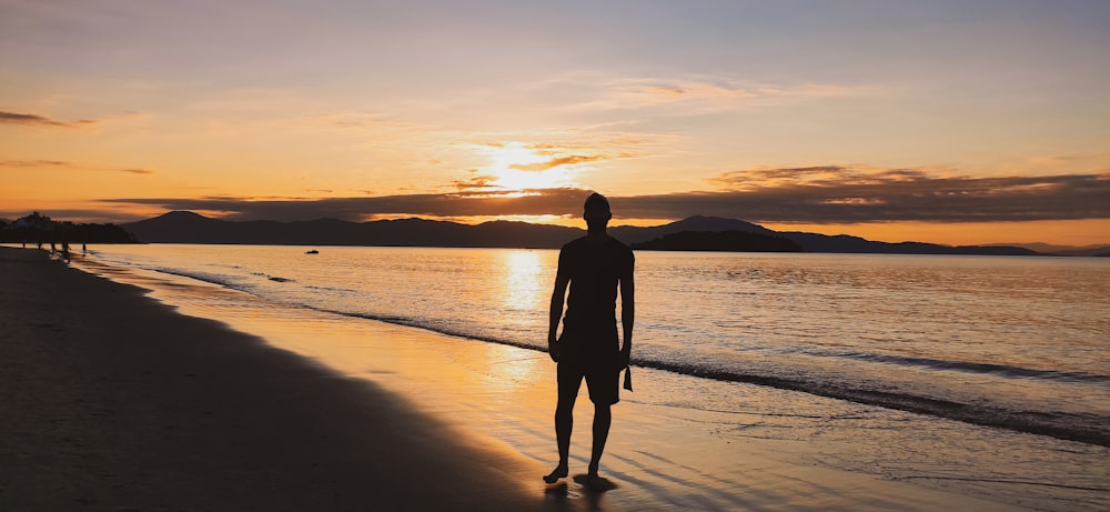 silhouette of man standing on seashore during sunset