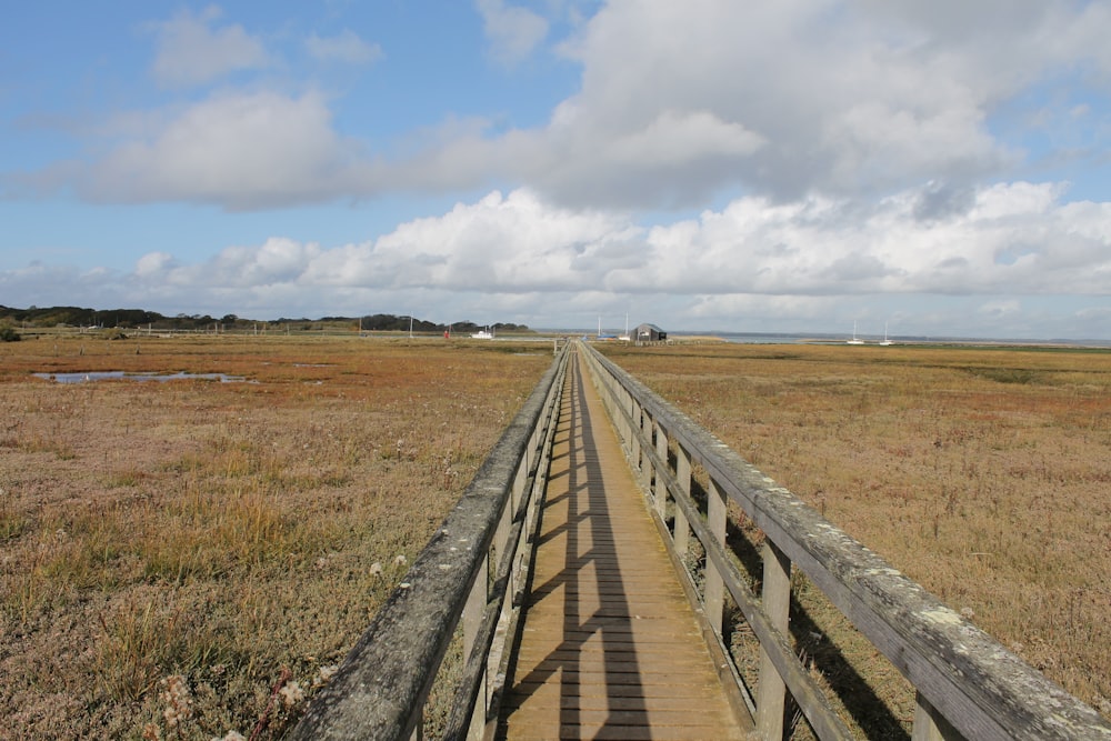 Braune Holzbrücke auf braunem Grasfeld unter weißen Wolken tagsüber