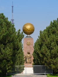 gold ball statue near green trees during daytime