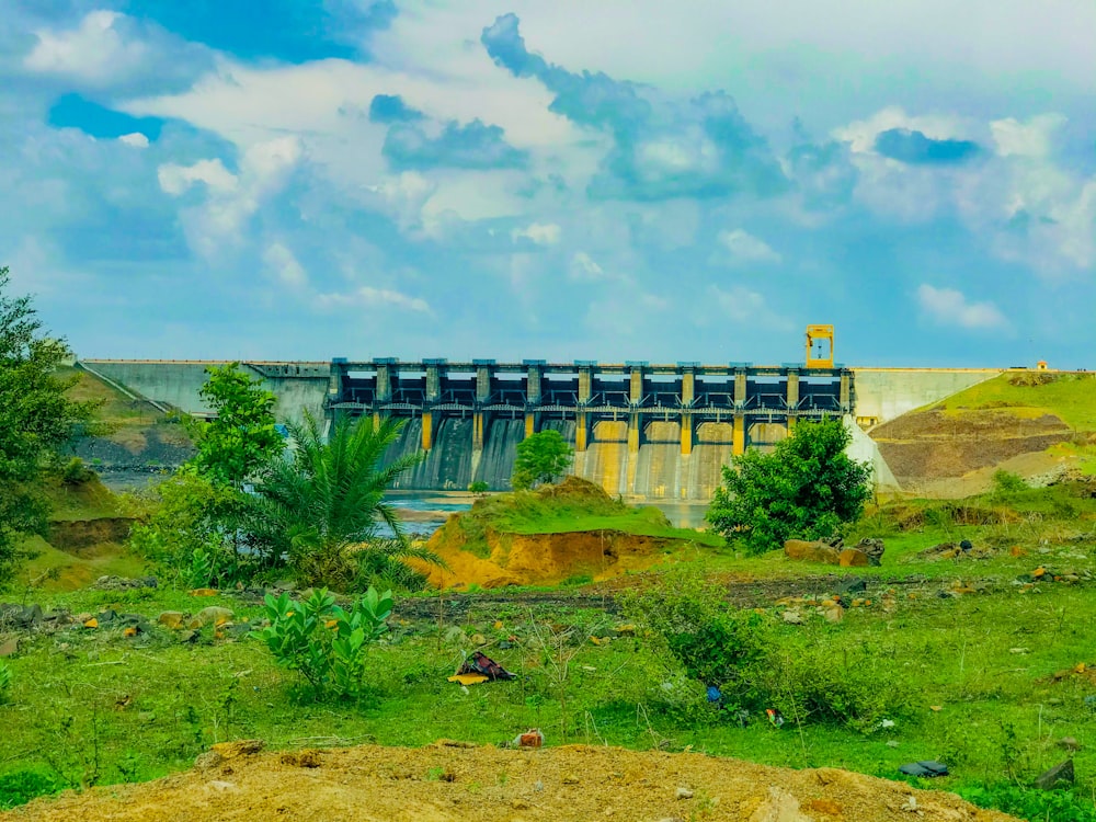 green grass field near gray concrete bridge under white clouds and blue sky during daytime