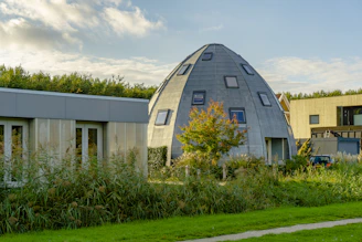 Modern wooden dome cabin with large windows in a green meadow during sunset.