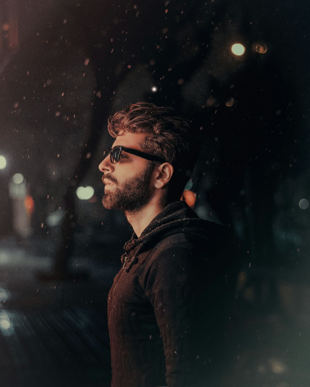 a man with a beard and sunglasses standing in the rain