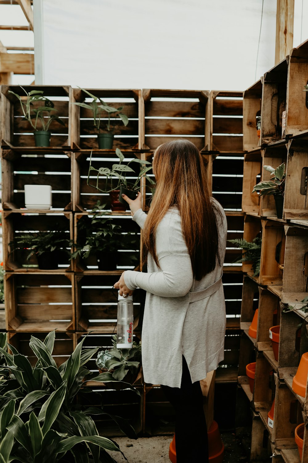 woman in white long sleeve shirt and gray skirt standing beside brown wooden shelf