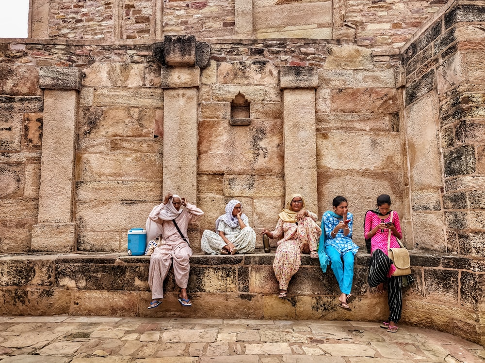 a group of people sitting next to each other on a stone wall