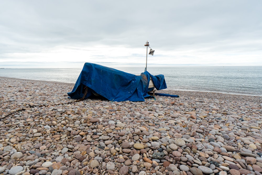 a blue tarp on a rocky beach next to the ocean