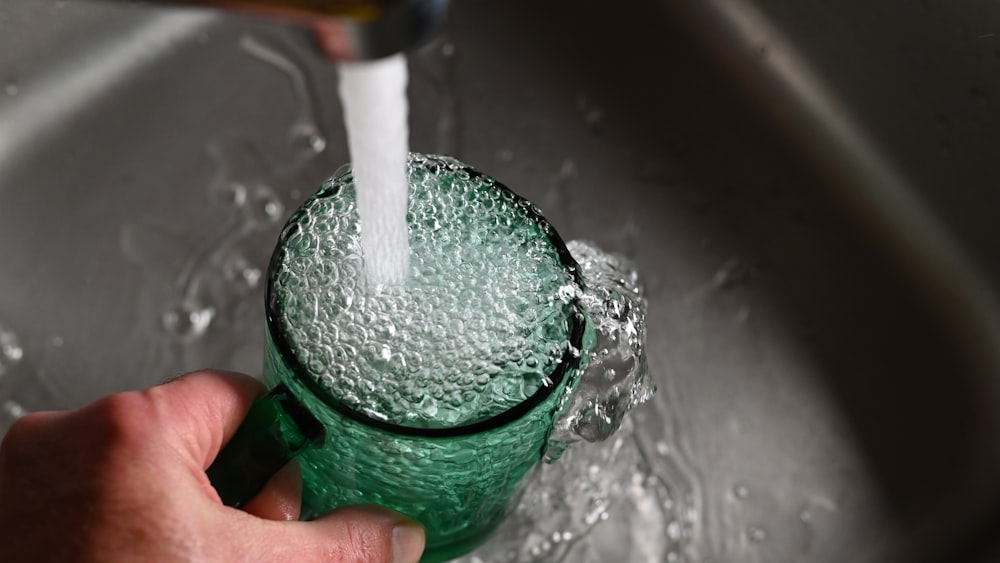 La mano di una persona tiene una tazza verde con l'acqua che esce da essa