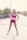 A woman stands confidently on a paved pathway surrounded by natural, sparse vegetation. She wears a bright pink athletic outfit consisting of a crop top and shorts, paired with white sneakers. Her stance is strong, with hands on her hips, looking to the side. The lighting is slightly overexposed, casting a soft and warm glow over the scene.