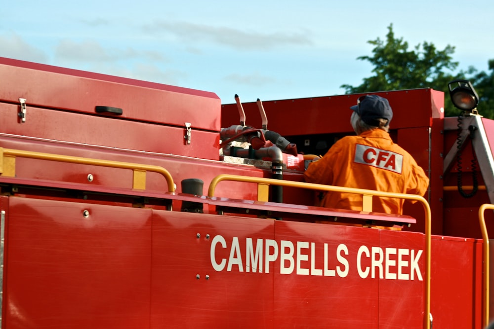 a man in an orange jacket is on a red fire truck