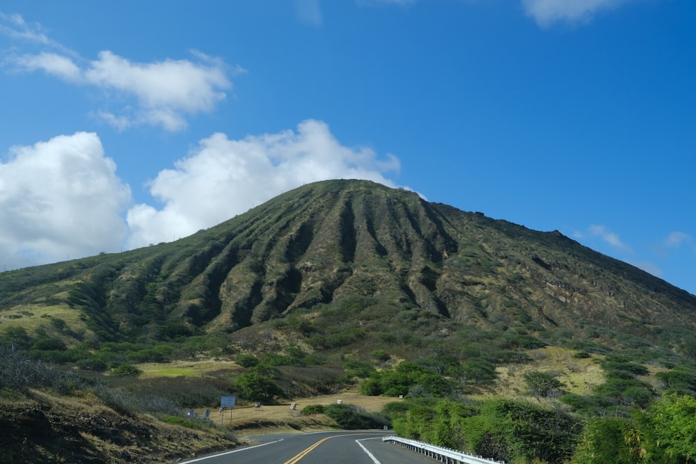 estrada de asfalto cinza perto da montanha verde sob o céu azul durante o dia