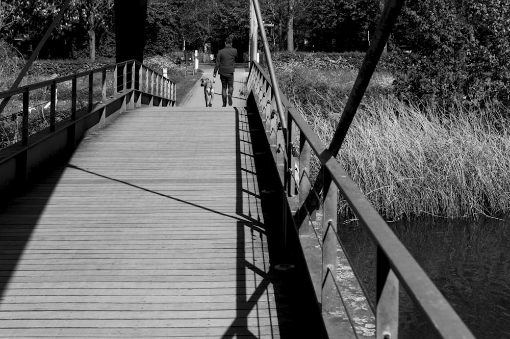 Photo en niveaux de gris de personnes marchant sur un pont en bois