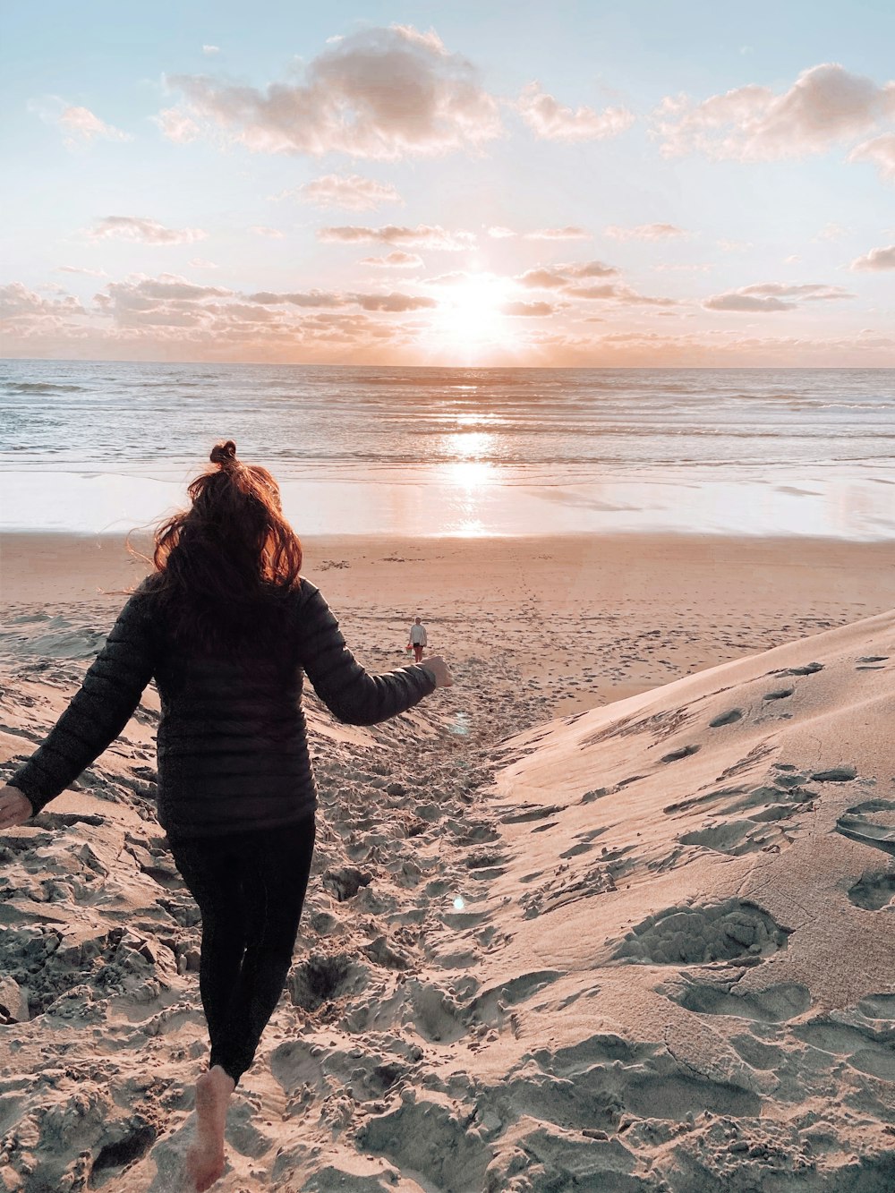 woman in black jacket and black pants standing on gray sand during daytime