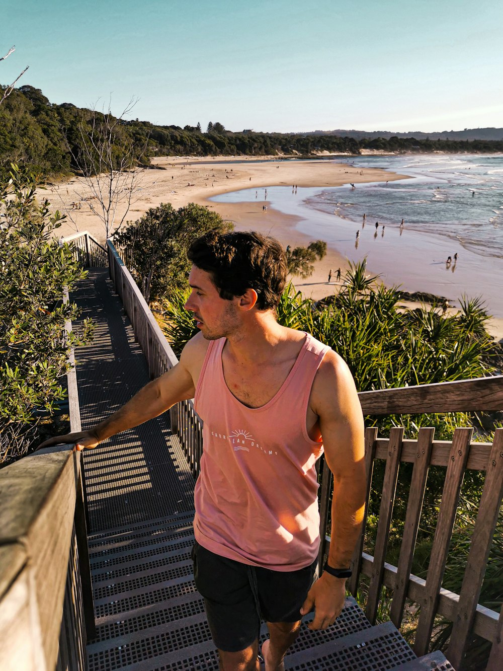 man in pink tank top standing on wooden dock during daytime