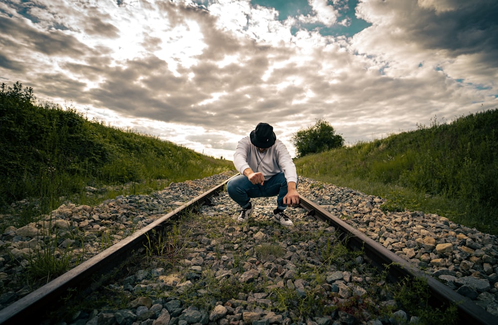 man in blue jacket and black pants sitting on train rail during daytime