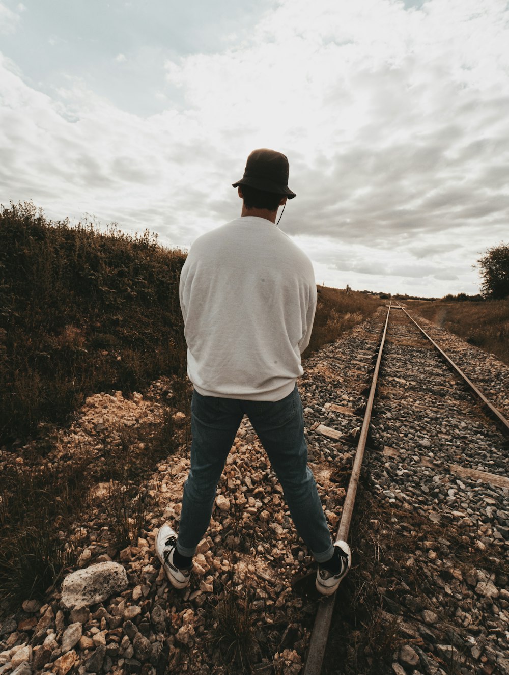 man in white shirt and blue pants standing on train rail during daytime