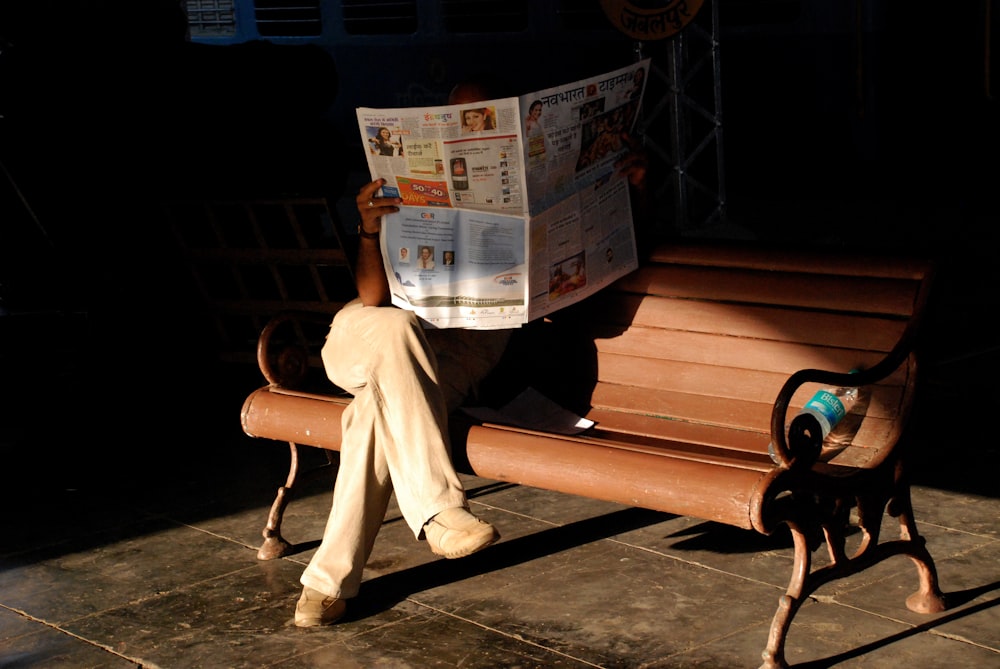 a person sitting on a bench reading a newspaper