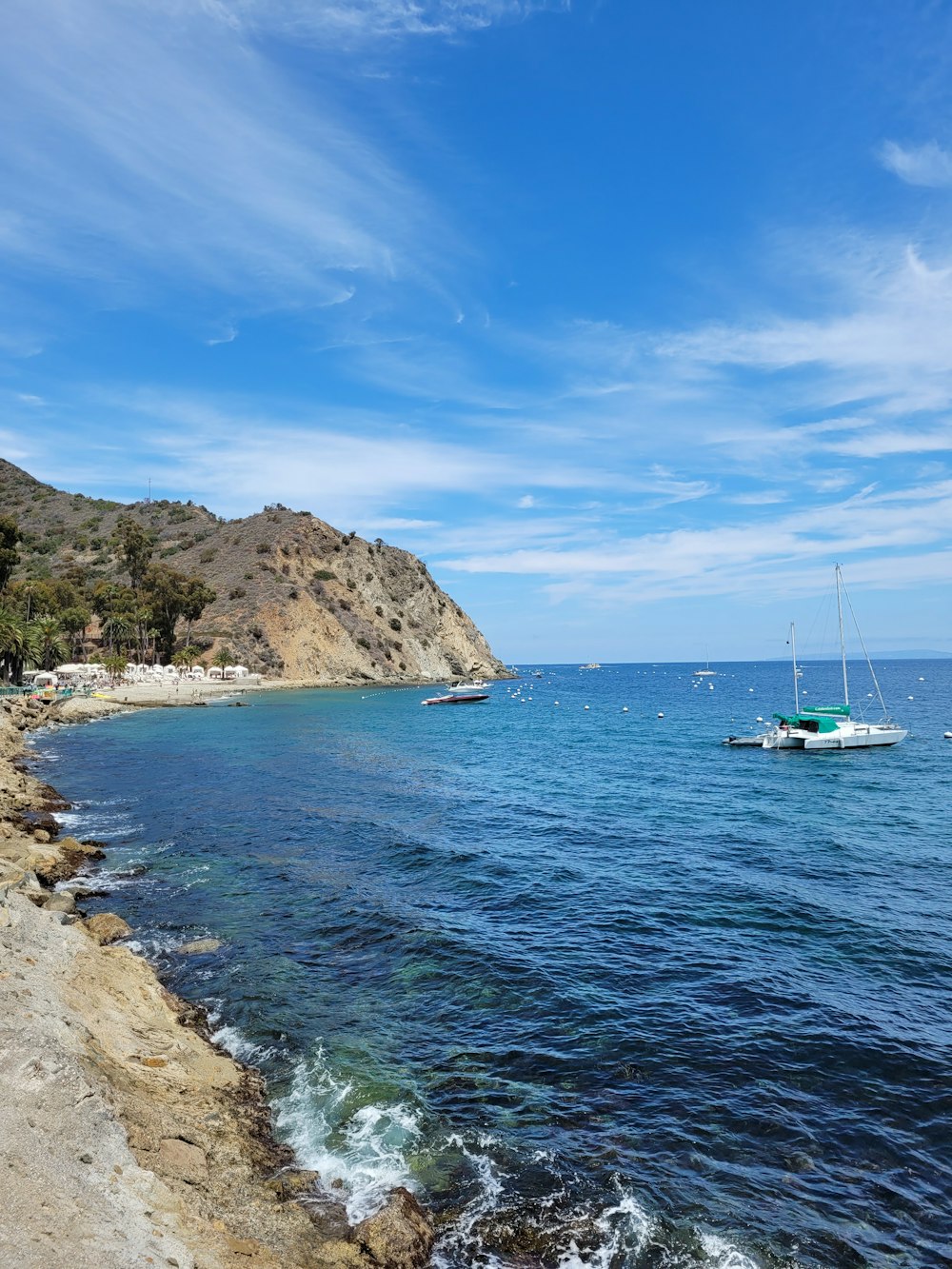 white boat on sea near brown rock formation under blue sky during daytime