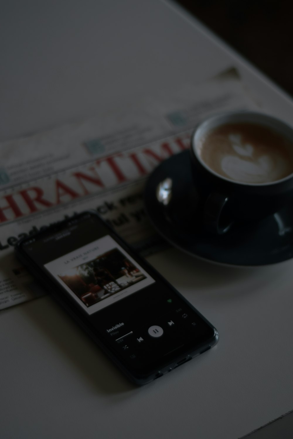 black ceramic mug on saucer beside black samsung android smartphone