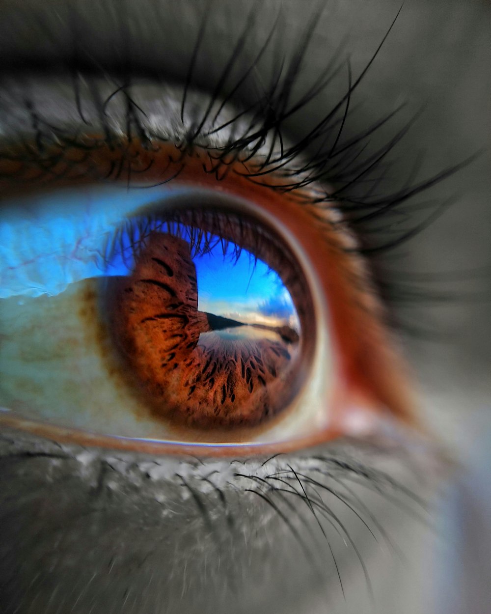 um close up do olho de uma pessoa com o reflexo do céu em