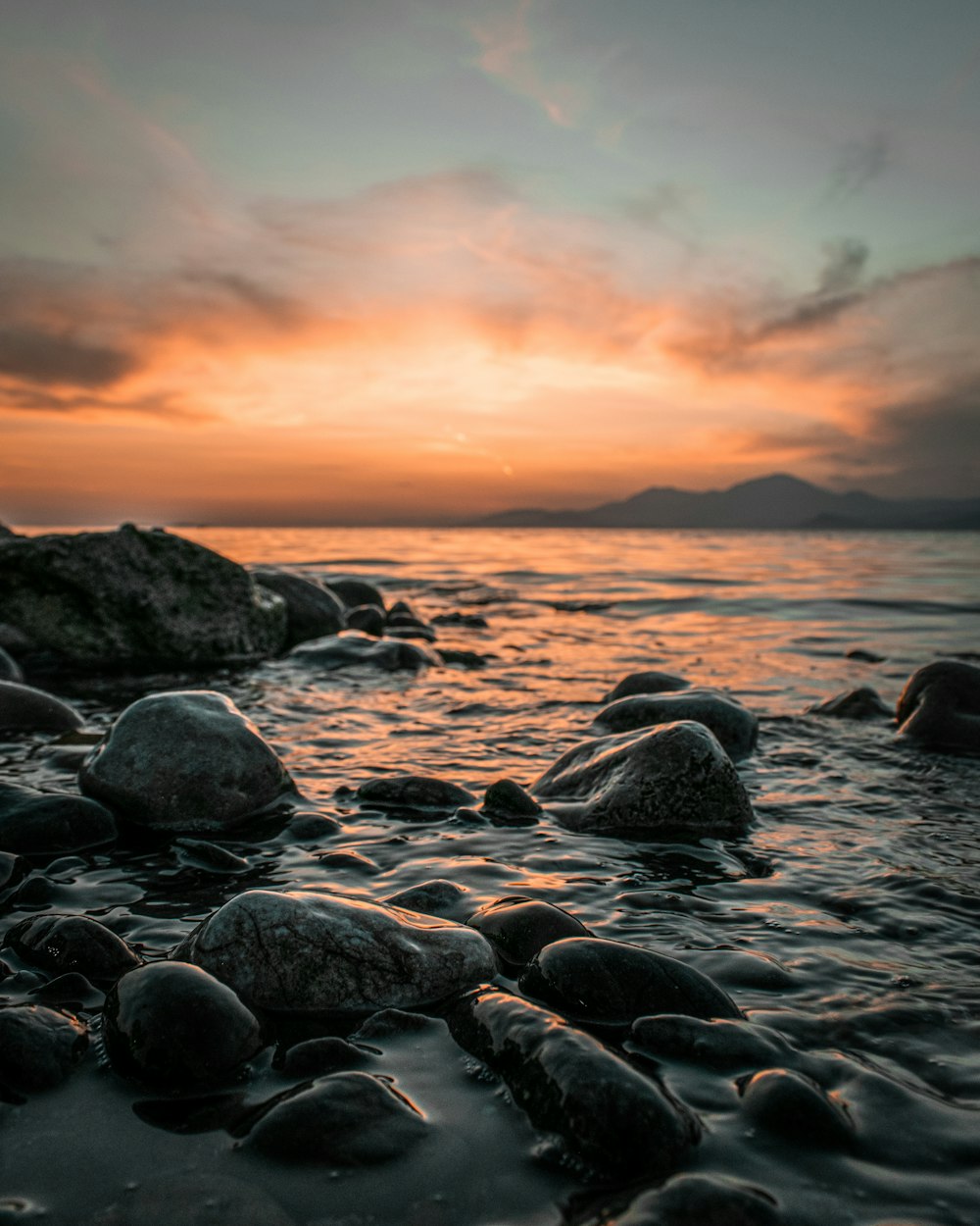 a sunset over the ocean with rocks in the foreground