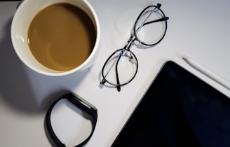 A cup of coffee next to a tablet with a tech blog open, surrounded by notes and a pair of glasses.