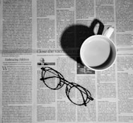 a cup of coffee and a pair of glasses on a newspaper