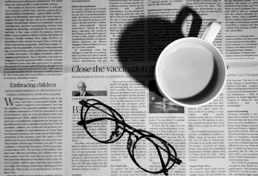 a cup of coffee and a pair of glasses on a newspaper