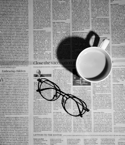 a cup of coffee and a pair of glasses on a newspaper