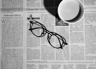 A cup of coffee with a pair of glasses on editorial page of newspaper.