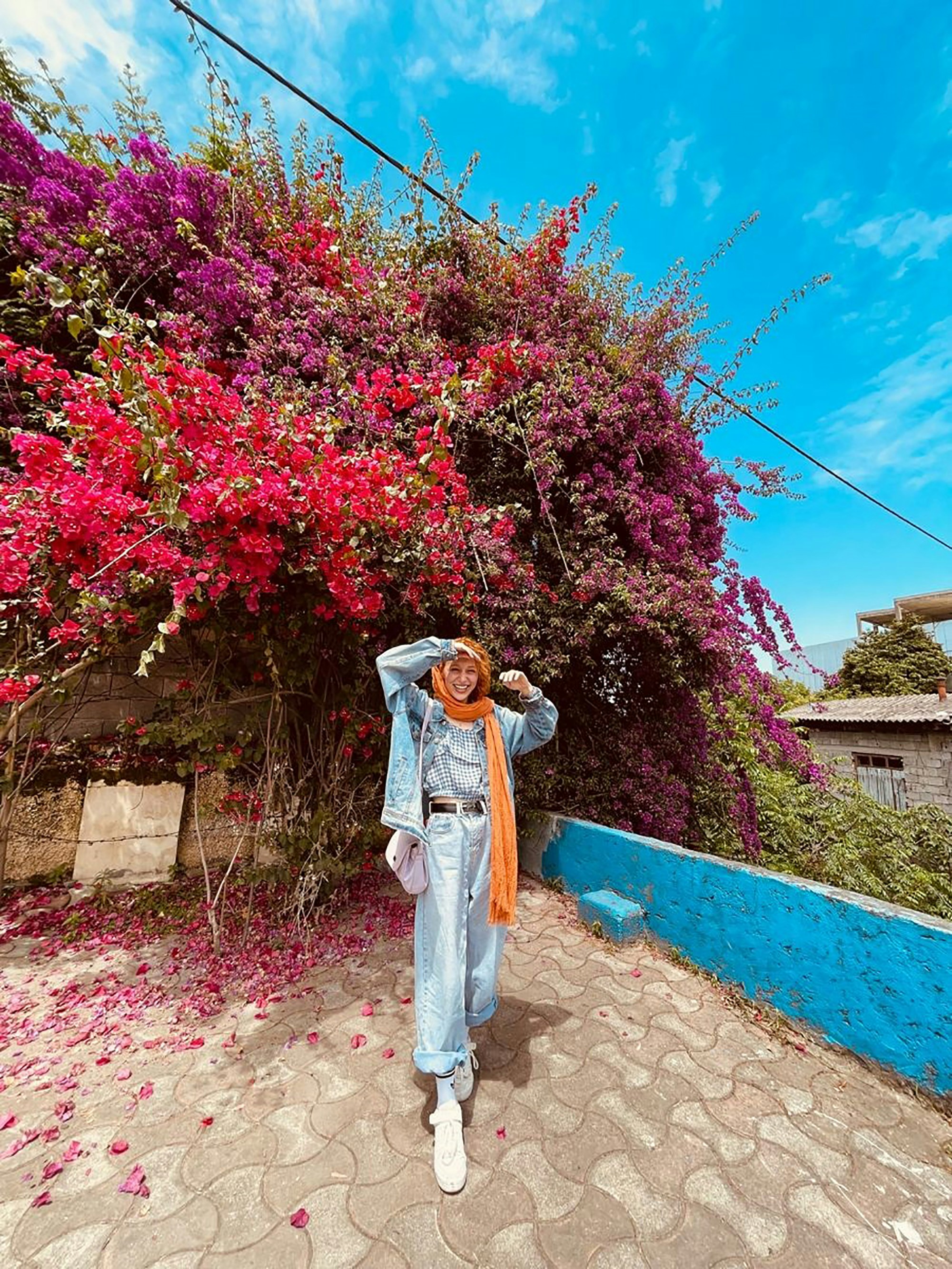 a woman standing in front of a bush with purple flowers