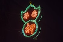 A glowing neon sign with intricate patterns, featuring Chinese characters lit in vivid orange and surrounded by a vibrant green chain-like border.