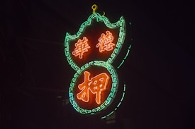 A glowing neon sign with intricate patterns, featuring Chinese characters lit in vivid orange and surrounded by a vibrant green chain-like border.