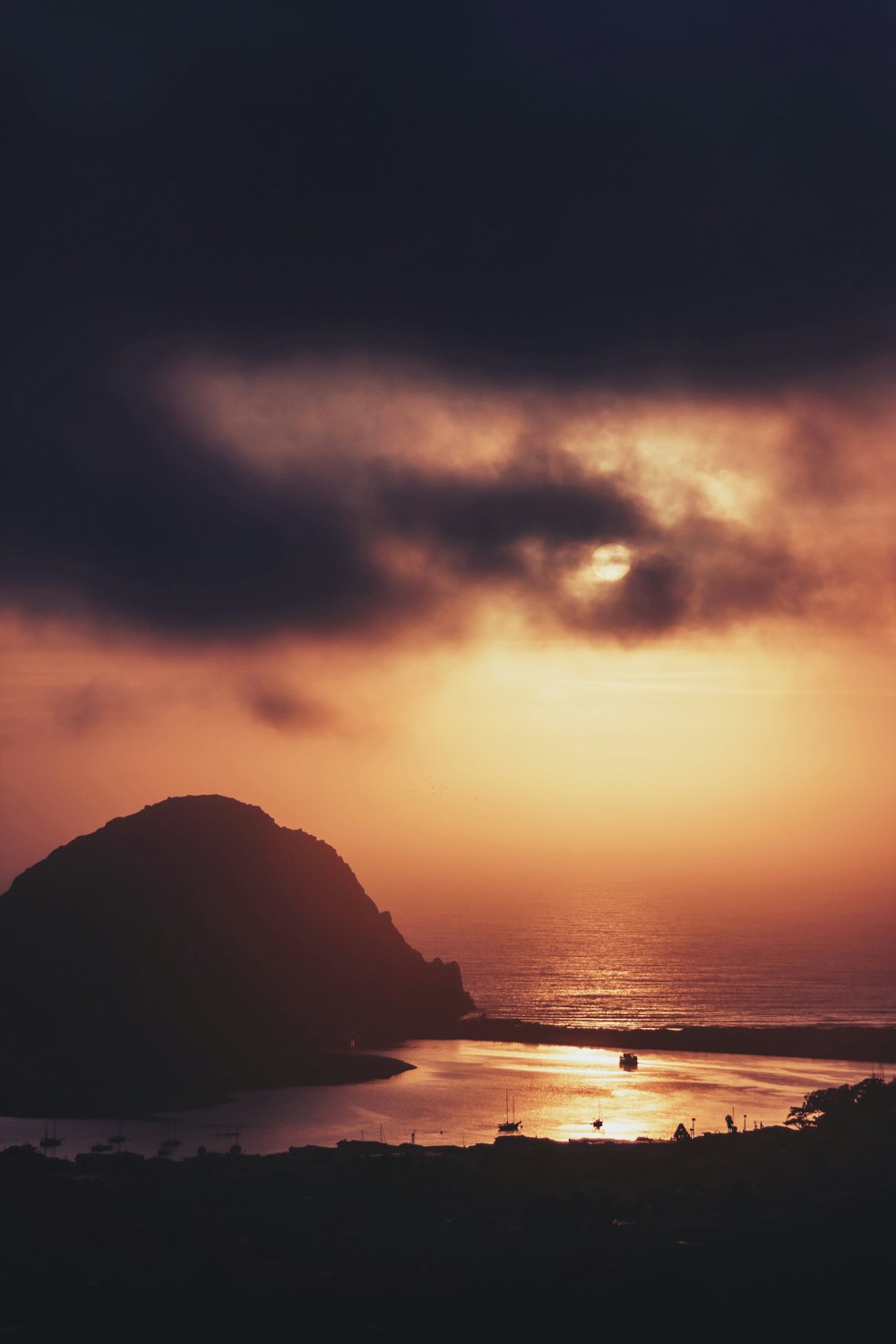 silhouette of mountain near body of water during sunset