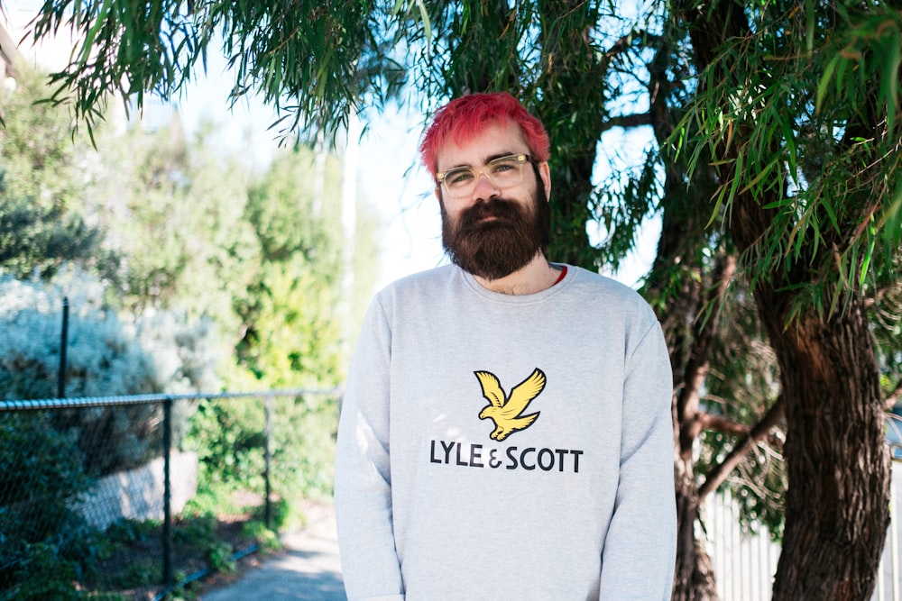 a man with red hair and a beard standing in front of a tree