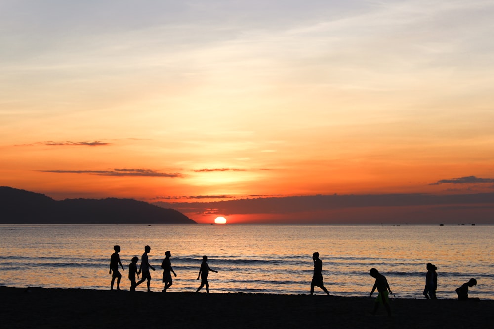 a group of people walking along a beach at sunset