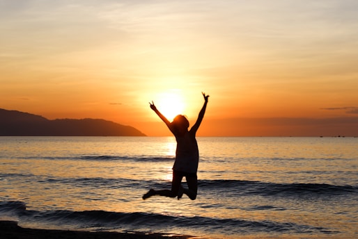 a happy person jumping into the air on a beach at dawn