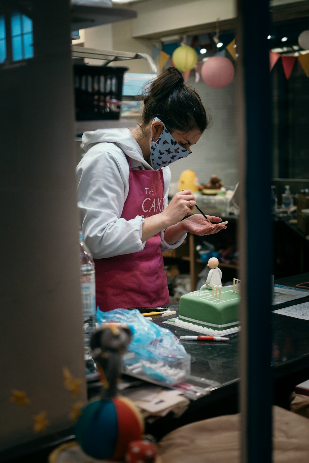 a woman wearing a face mask is decorating a cake