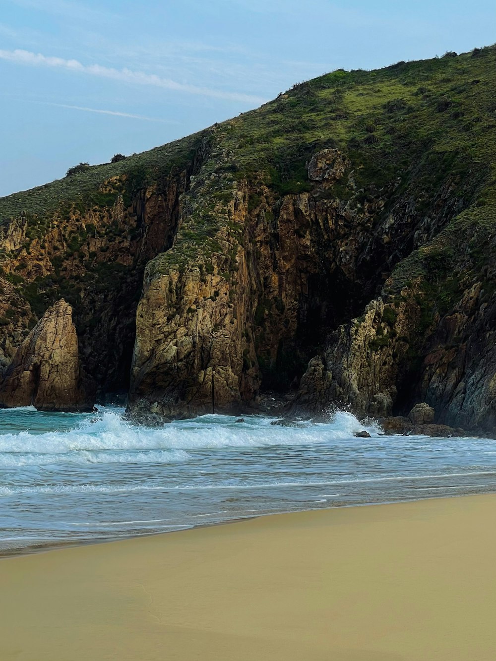 a sandy beach next to a rocky cliff