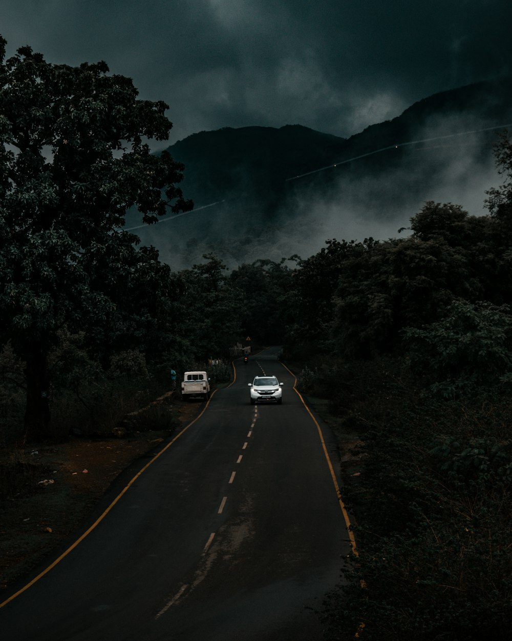 a couple of cars driving down a road under a cloudy sky