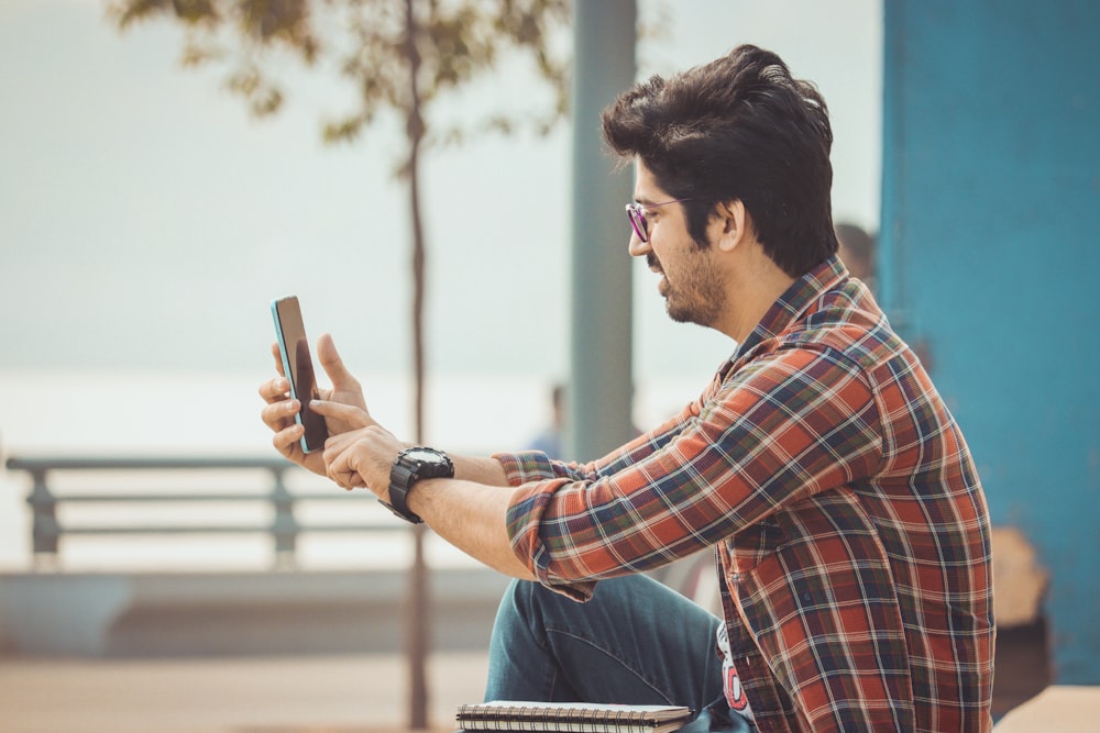 Un hombre sentado en un banco mirando su teléfono celular