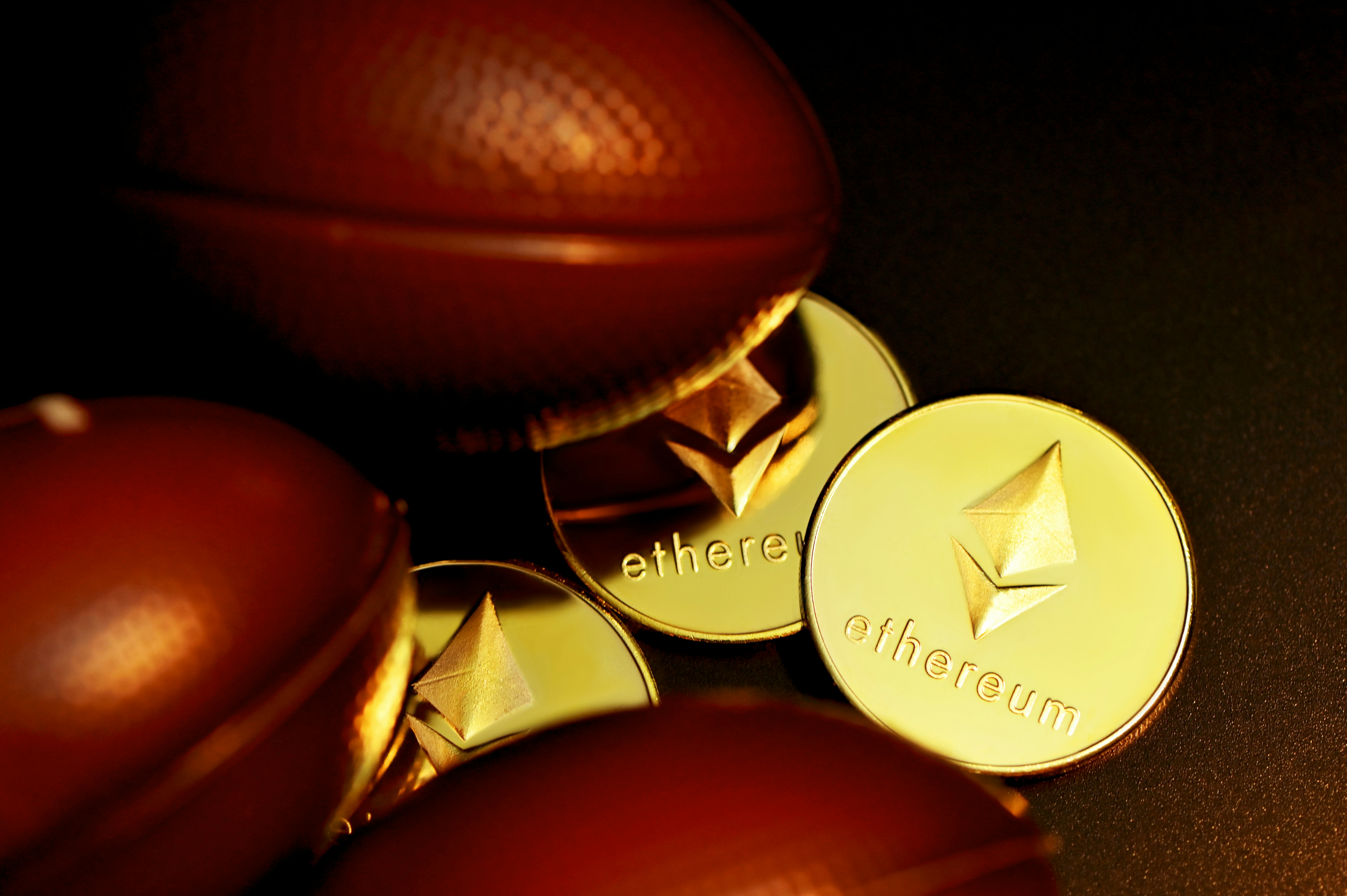 Three Ethereum coins and next to some footballs on the floor.
