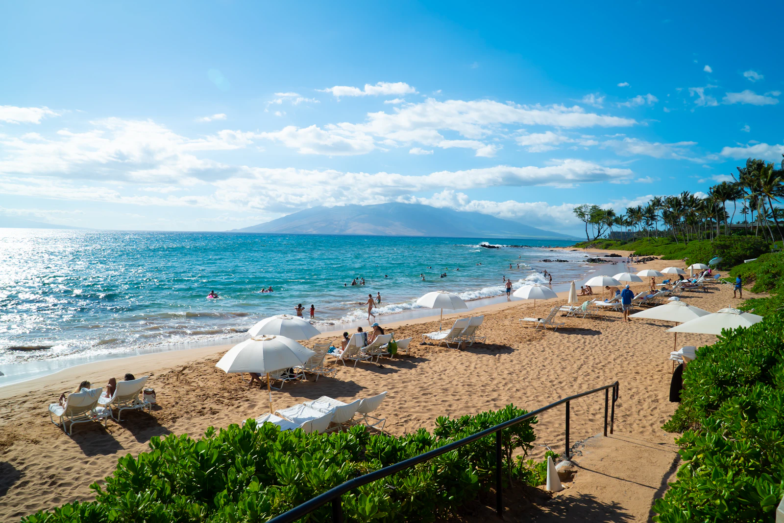 White parasols along the sand at a Maui beach, the headland beyond