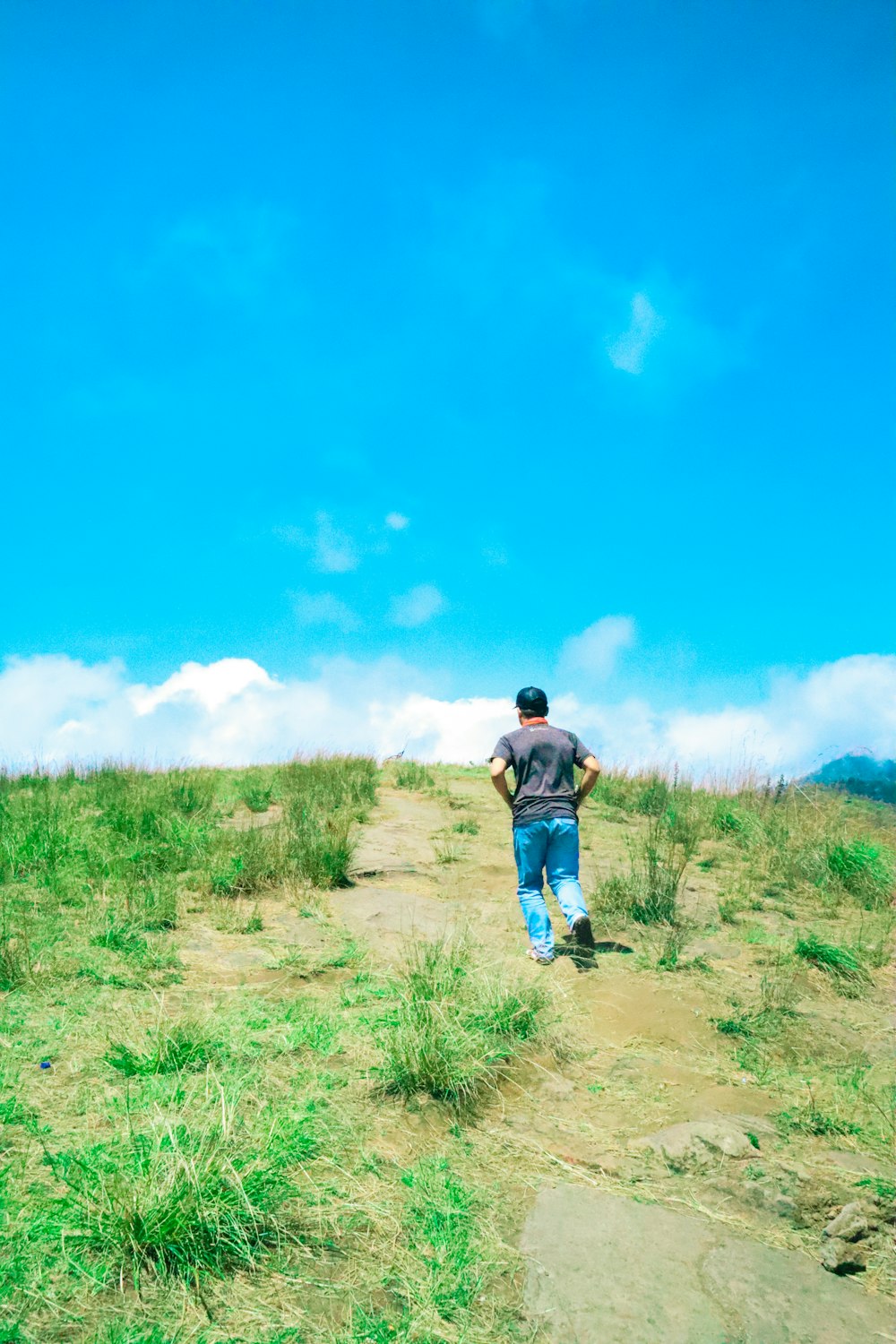 a man walking down a dirt road next to a lush green field